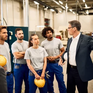 homme-d-affaires-d-age-moyen-donnant-une-presentation-a-un-groupe-de-travailleurs-industriels-dans-u
